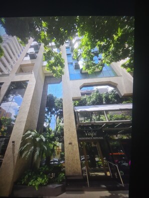 A modern building with a glass facade, a visible entrance with a sign, and surrounding greenery. - LIBERDADE SQUARE SAVASSI/LOURDES (Belo Horizonte)