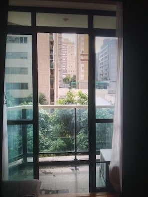 A room with a large window, a balcony, and a view of tall buildings and greenery. - LIBERDADE SQUARE SAVASSI/LOURDES (Belo Horizonte)