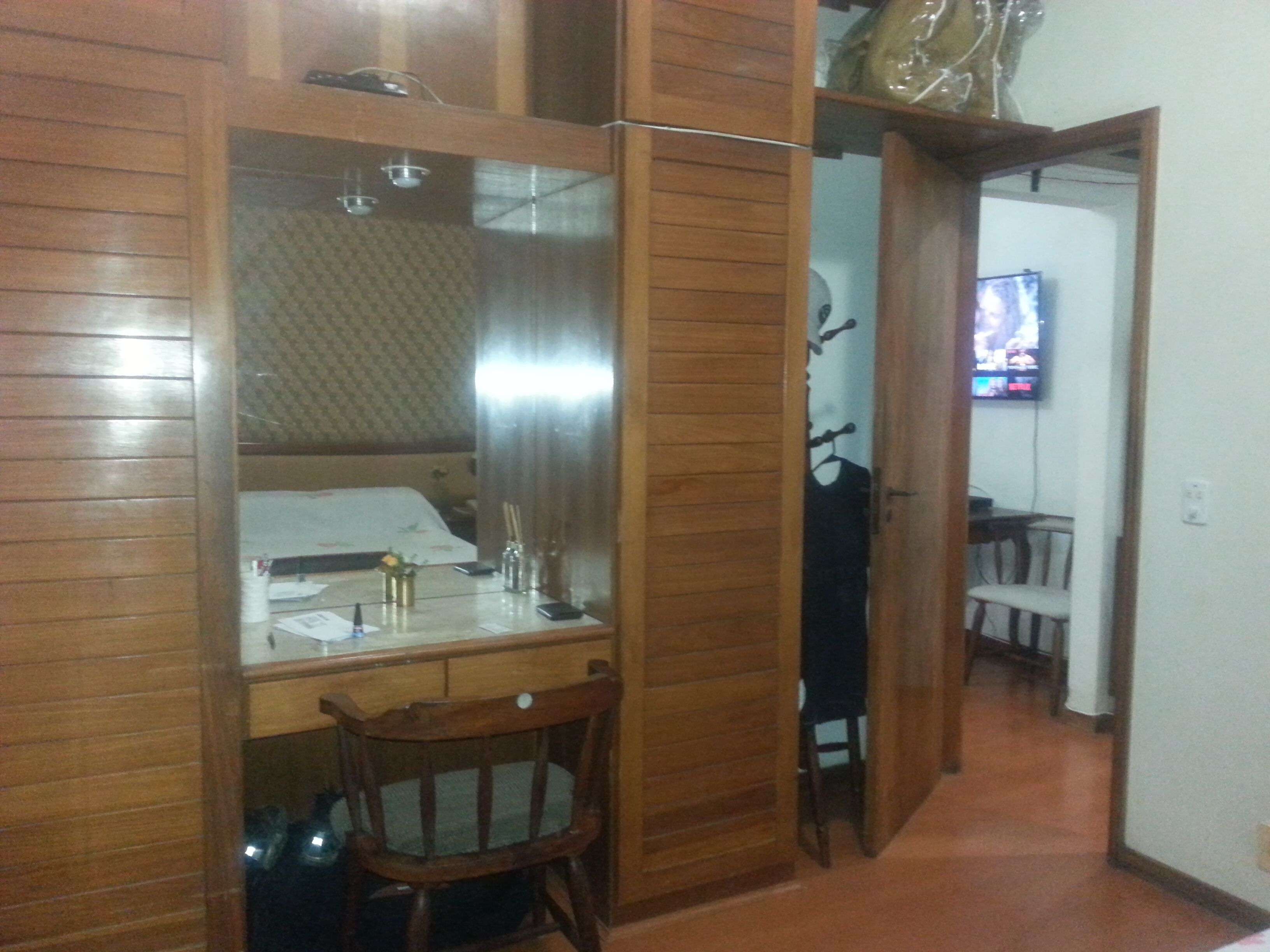 Een hotelkamer met een houten bureau, een stoel, een bed en een televisie op de achtergrond.
