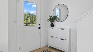 Eine weiße Tür mit Fenster, ein weißes Konsolenmöbel mit Schubladen, ein runder Spiegel und ein Blumentopf.
