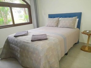 A bed with a blue headboard, a bedside table, and a window with a view of greenery. - Flor de Palma Villa (Tronadora)