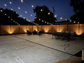 An outdoor patio area with string lights, a wooden fence, and outdoor furniture.