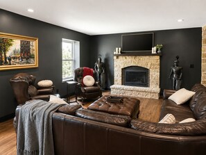 A living room with a stone fireplace, leather sofas, a large painting, and two statues.