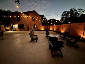 Un patio al aire libre con paredes de ladrillo, luces colgantes y mobiliario exterior.