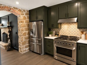 Una cocina con arco de piedra, electrodomésticos de acero inoxidable y armarios color verde oscuro.