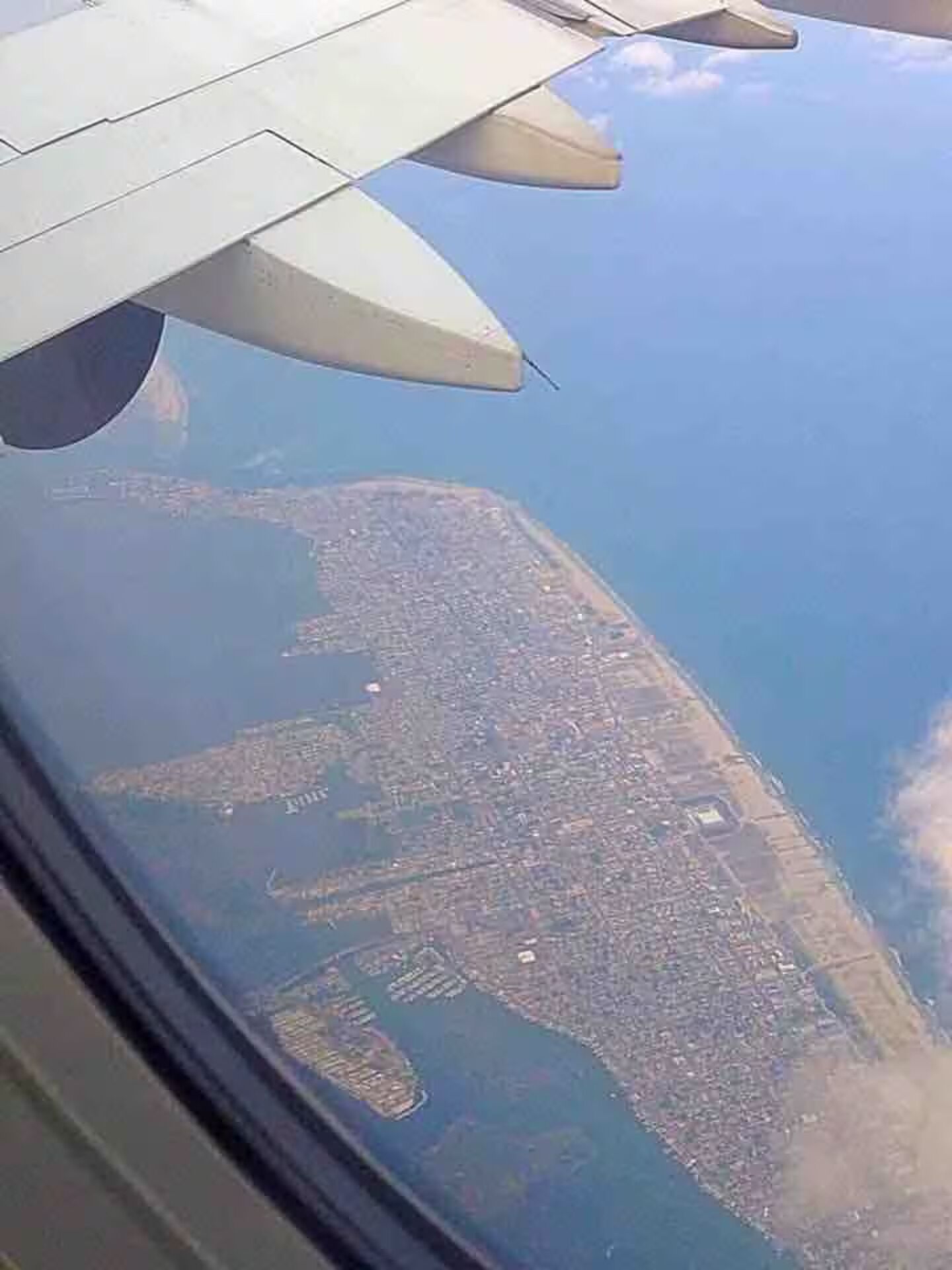 An aerial view of a coastal city with a dense urban layout, a large body of water, and a clear sky.