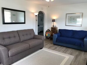 A living room with two sofas, a rug, a lamp, a framed map, and a wall-mounted mirror.