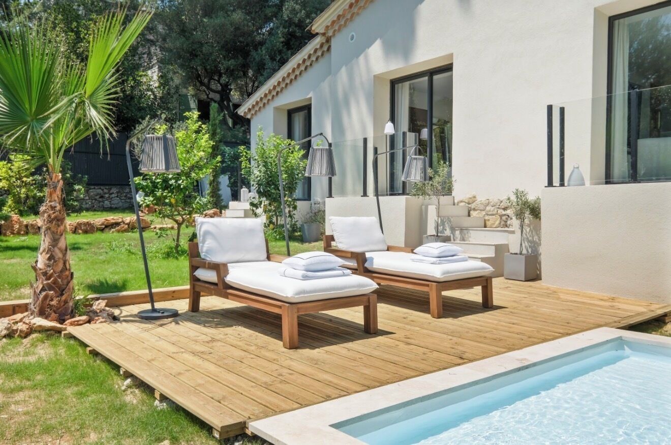Un espace piscine extérieur moderne comprenant deux chaises longues, une terrasse en bois et une petite piscine.