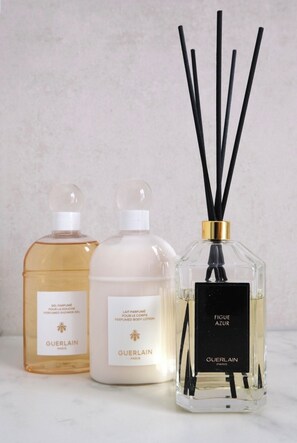 Três frascos de perfume Guerlain com fragrâncias distintas e um difusor com palhetas pretas.
