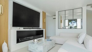 A modern living room with a large flat-screen TV mounted on a white wall, a white sofa, a marble coffee table, and a minimalist decor style. - Stunning Villa in Cap d'Antibes for 6 Guests, Ocean View, Air Conditioning (Antibes)