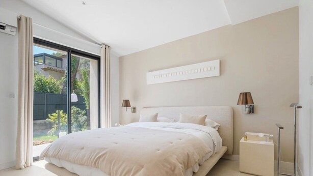 A modern bedroom with a large bed, a bedside table, a floor lamp, and a view of the outdoors. - Stunning Villa in Cap d'Antibes for 6 Guests, Ocean View, Air Conditioning (Antibes)