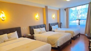 Habitación de hotel con tres camas, piso de madera e iluminación instalada en la pared.