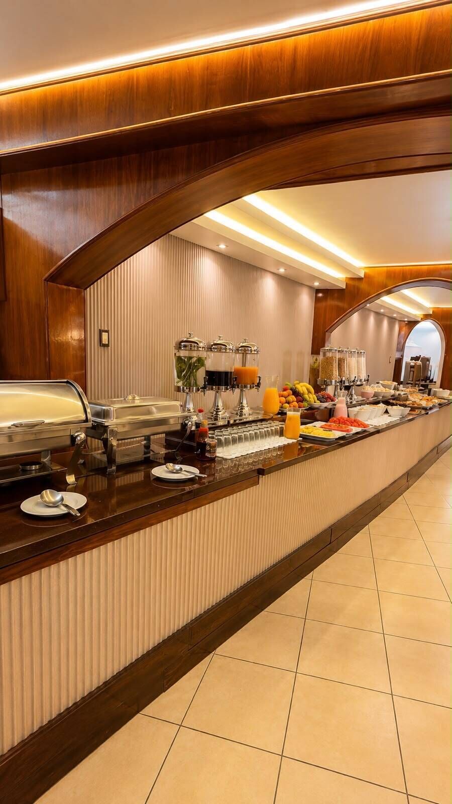 Disposição de buffet com diversos alimentos e bebidas, incluindo frutas, cereais e um espaço para café.