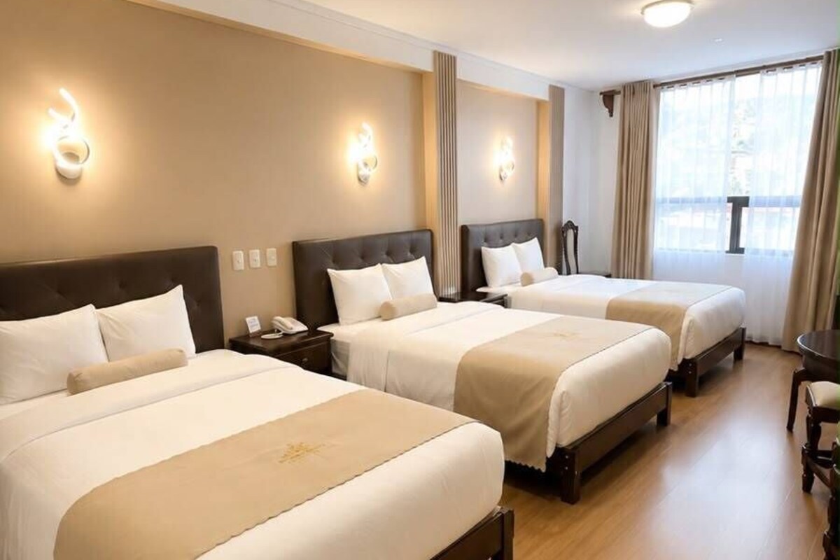 A hotel room with three beds, a wooden floor, and a large window with curtains.
