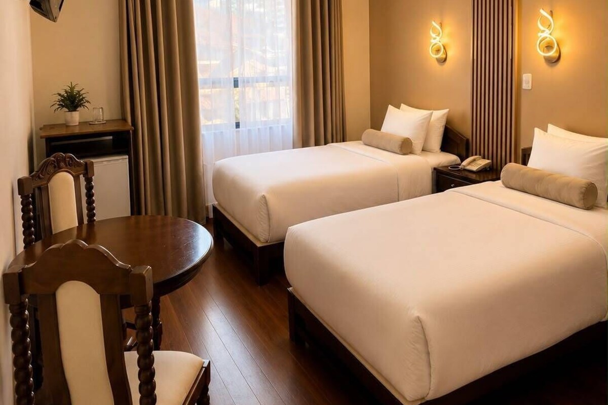 A hotel room with two beds, a desk, a chair, and a television.