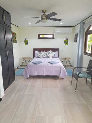 Ein Schlafzimmer mit einem Bett, zwei Nachttischen, einem Deckenventilator, einer Klimaanlage und einem Fenster mit Vorhängen.