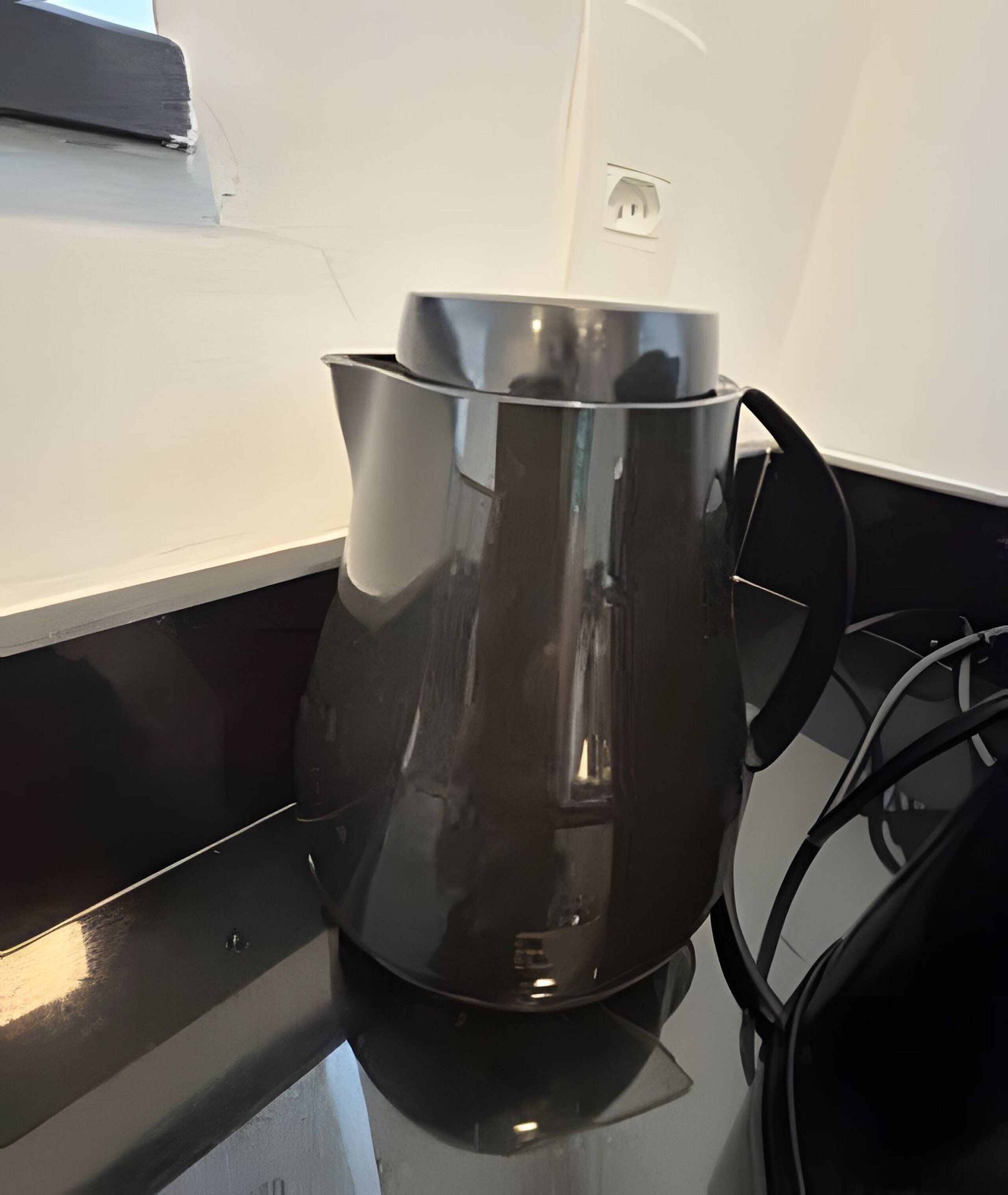 A stainless steel kettle on a black countertop with a power outlet in the background.