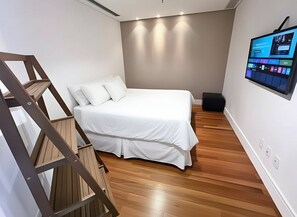 Un dormitorio con cama, televisor montado en la pared y suelo de madera.