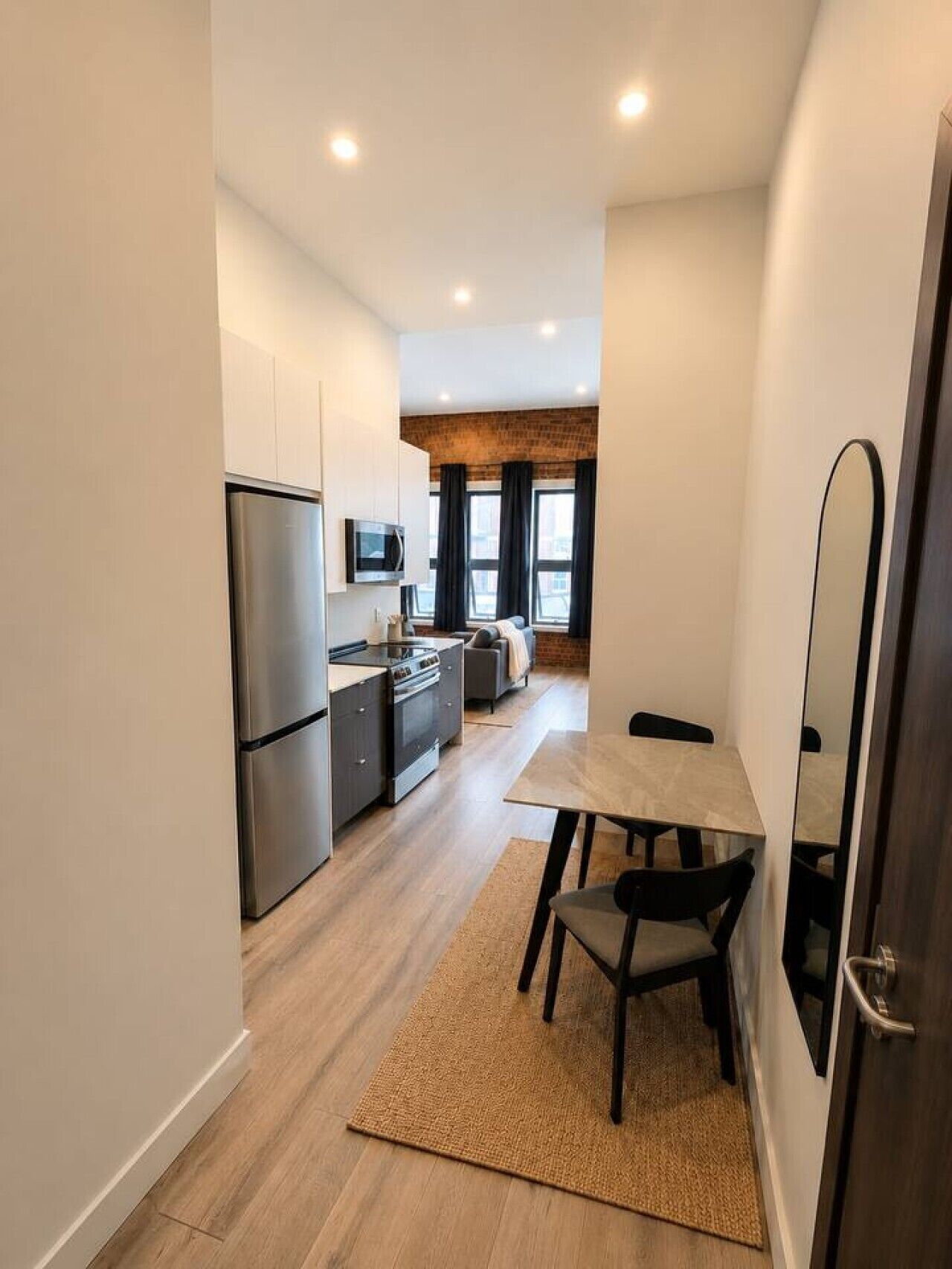 Una cocina compacta con electrodomésticos modernos, un comedor con mesa y sillas, y vista al salón a través de un vano.