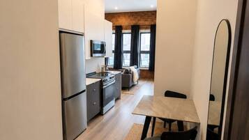 Una cocina compacta con electrodomésticos modernos, un comedor con mesa y sillas, y vista al salón a través de un vano.