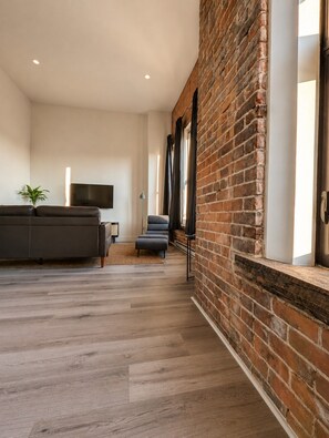 A modern living room with a brick wall, a sofa, a TV, and a window. - Boutique Suite in Historic Downtown Renfrew (Renfrew)