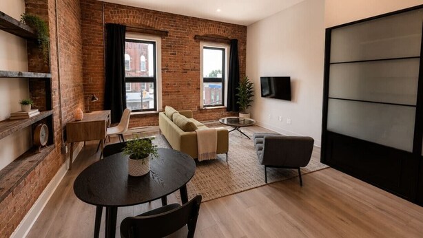 Un salón moderno con pared de ladrillo, un sofá, una mesa de centro y un televisor montado en la pared.