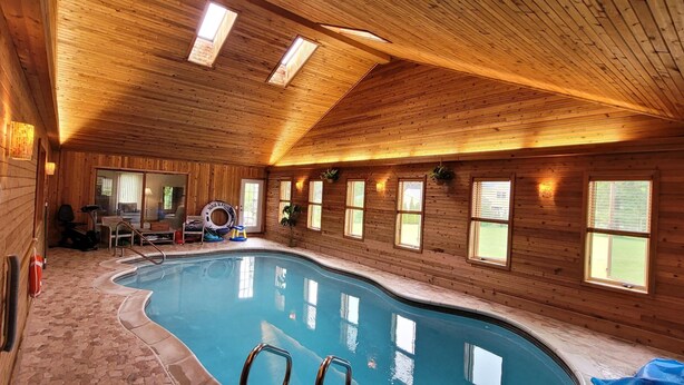 An indoor swimming pool with wooden walls and ceiling, surrounded by windows. - Luxury Home with Indoor Pool, 3-bedroom house in delightful Milford MI (Milford)