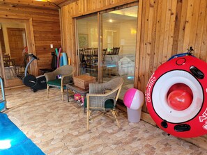 Ein Holzblock-Innenraum mit Korbmöbeln, einer Glastür, die nach draußen führt, und einem roten Schwimmreifen.