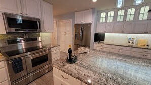 A kitchen with stainless steel appliances, white cabinetry, and a marble countertop. - Luxury Home with Indoor Pool, 3-bedroom house in delightful Milford MI (Milford)