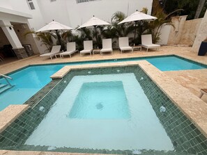 Ein rechteckiger Pool mit Fliesenbordur, umgeben von Liegestühlen und Sonnenschirmen.