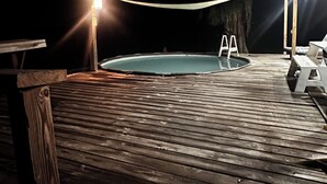 Una terraza de madera con un jacuzzi y una mesa, iluminada por una sola fuente de luz.