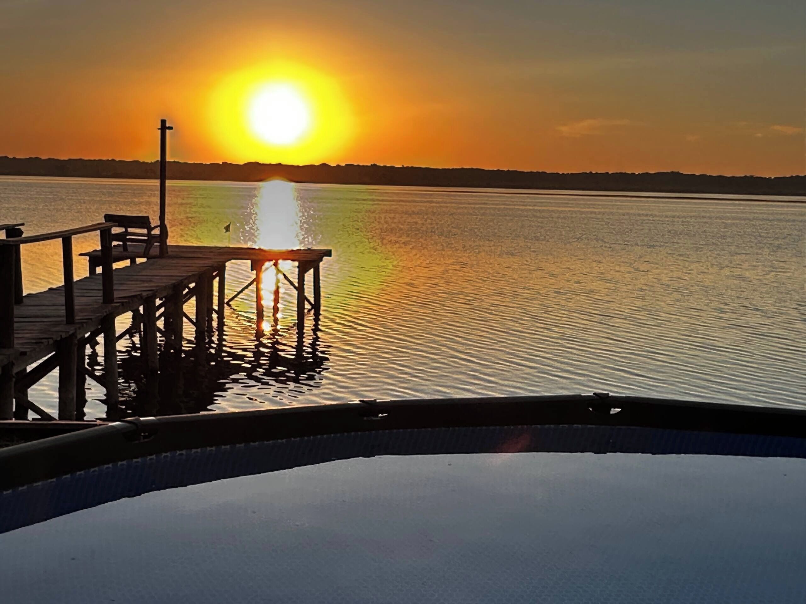 A wooden pier extending into calm water with a sunset in the background.