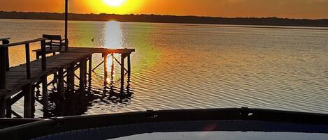 A wooden pier extending into calm water with a sunset in the background.