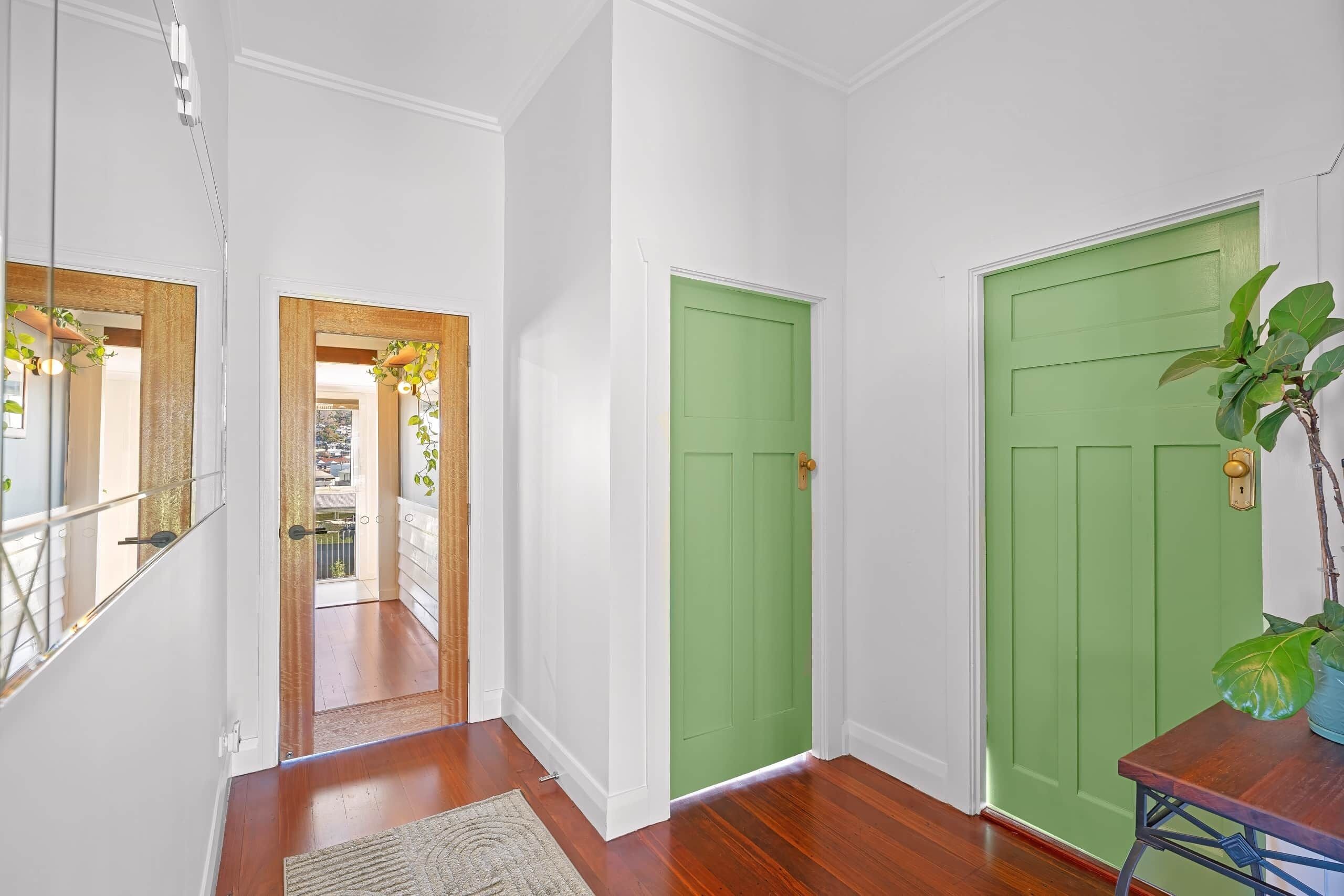 A hallway with wooden flooring, white walls, and two green doors.