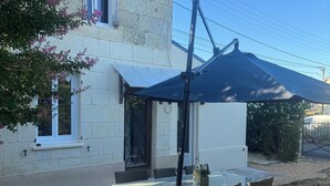 Eine Terrasse mit Tisch und Stühlen, einem schwarzen Sonnenschirm und einem Haus mit Steinwänden und einem Fenster.