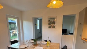 Ein Essbereich mit einem Holztisch, vier Stühlen, einer transparenten Tischdecke, einer Flasche und einem gerahmten Bild an der Wand.