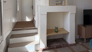 Ein Flur mit einer Treppe, einem Kamin und einem Spiegel darüber sowie einem Fernseher auf einem Schrank.