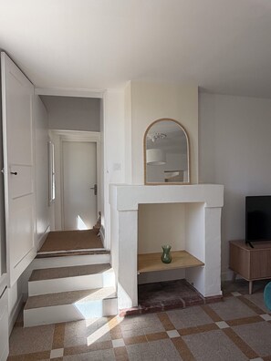 A hallway with a staircase, a fireplace with a mirror above it, and a television on a stand. - Cozy House (Saumur)