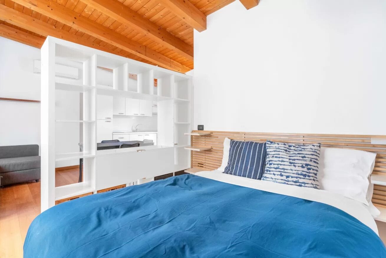A bedroom with a bed, a white wardrobe, a grey sofa, and a wooden ceiling.