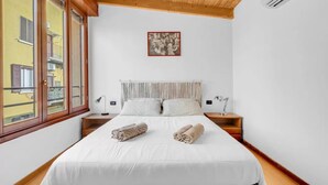 Una camera da letto con un letto grande, due comodini, una finestra vista edifici e un quadro appeso al muro.
