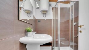 Un bagno moderno con un lavandino bianco, un box doccia in vetro e una pianta in vaso.
