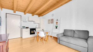 Una cucina moderna con mobili bianchi, un tavolo da pranzo con sedie, un divano grigio e un soffitto in legno.