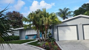 A residential garage with a white door, a small garden with flowers and plants, and a blue chair outside. - Stylish Pool Retreat in the Heart of Vero Beach. (Vero Beach)