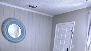 A room with two white armchairs, a round mirror, a door, and a small table with a lamp. - Stylish Pool Retreat in the Heart of Vero Beach. (Vero Beach)