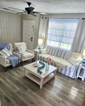 Ein Wohnzimmer mit einer Couch, Sesseln, einem Couchtisch und einem Deckenventilator.