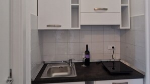 Et kompakt køkken med hvide skabe, en sort bordplade og en stålvask.