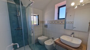 Et badeværelse med brusekabine i glas, toiletbidét og vask med træbordplade.