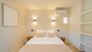 A bedroom with a bed, two wall-mounted lights, an air conditioner, and a small window.
