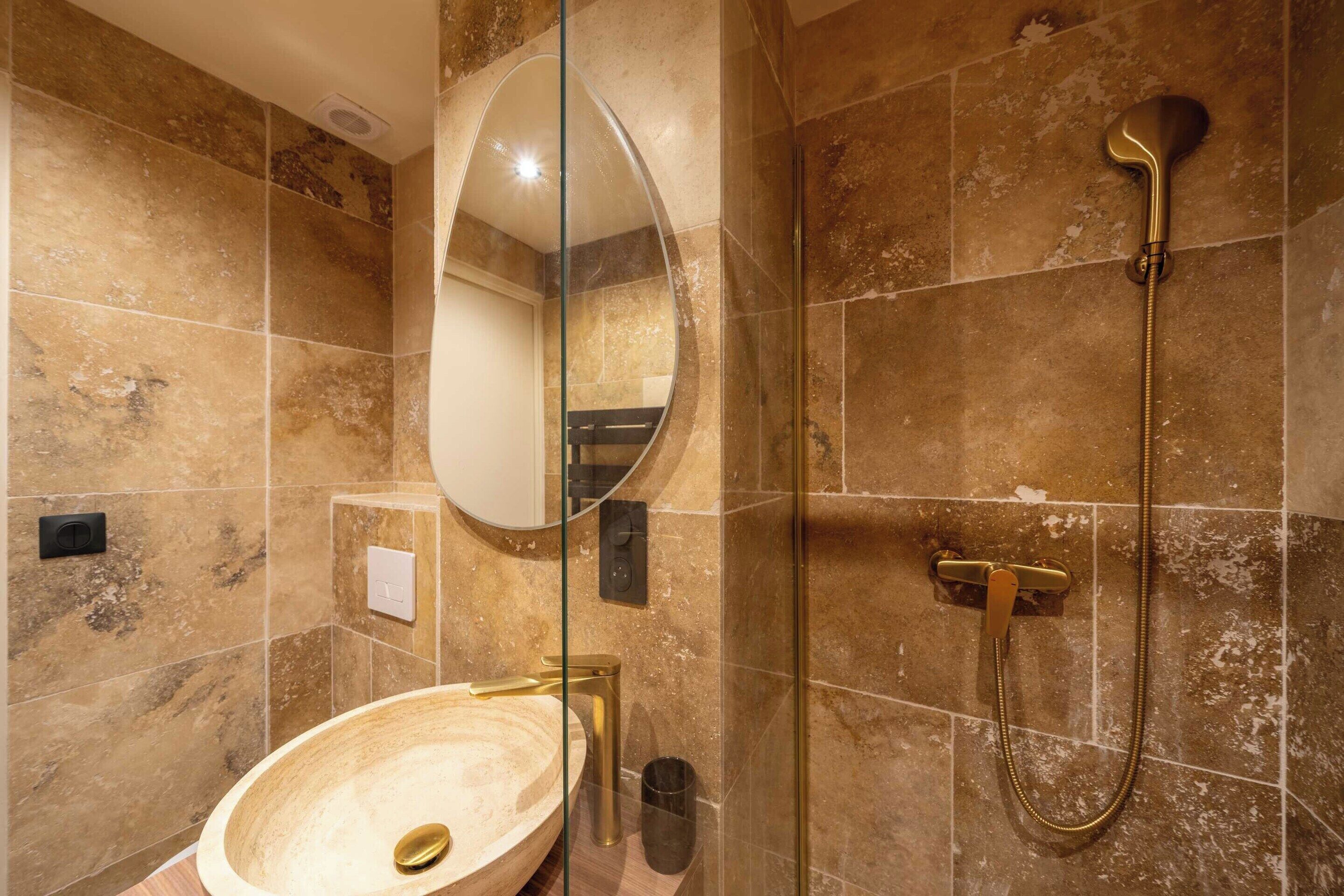 Een badkamer met een rond wastafel, een douche met glazen wanden en een grote spiegel.