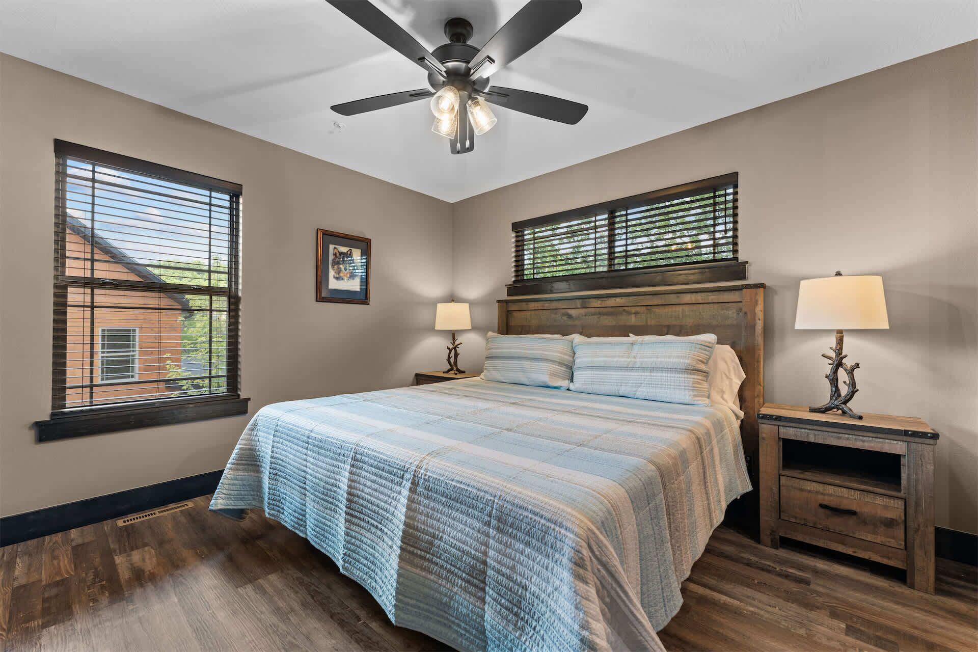Un dormitorio con una cama, dos mesitas de noche, un ventilador de techo y ventanas.